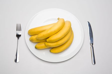 Bunch of bananas placed on the plate with fork and knife near byの写真素材