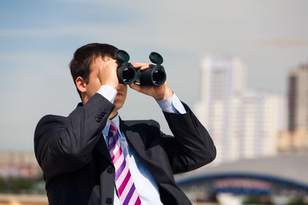 Portrait of handsome businessman with binoculars in hands looking through it in the downtownの写真素材