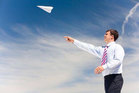 Image of businessman letting paper airplane fly and looking at it on background of blue skyの写真素材