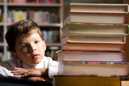 Face of diligent schoolboy looking at stack of books in the library