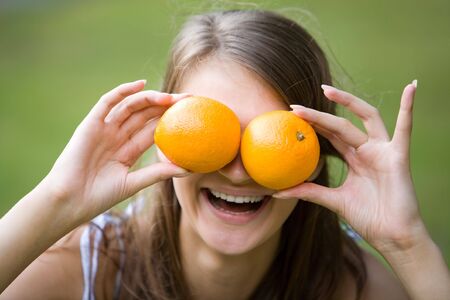 Face of joyful girl holding oranges by her eyes and laughingの写真素材