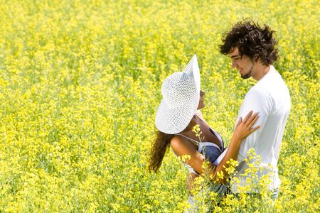 Photo of happy couple embracing on meadow of yellow flowers at summertime