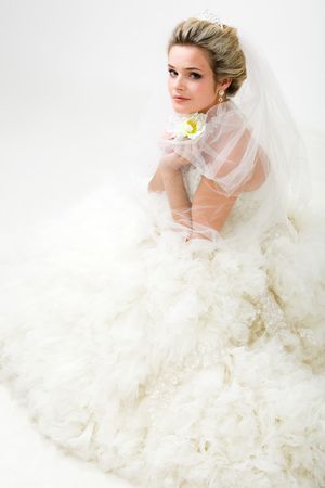 Photo of elegant bride in fashionable wedlock with flower in hand sitting and looking at cameraの写真素材