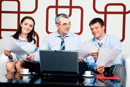 Adult businessman sitting at the table and giving documents to managers の写真素材