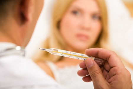 Close-up of doctor’s hand holding thermometer with sick woman on background