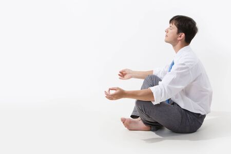 Meditating man sitting in pose of lotus in profile over white backgroundの写真素材