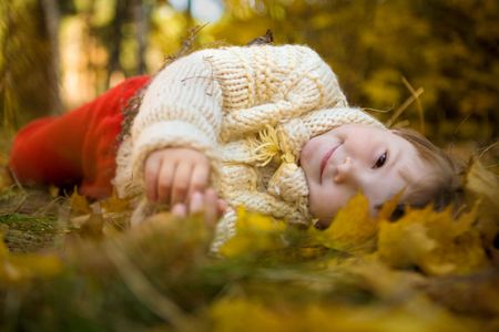 Cheerful girl lying on her side surrounded by leaves and looking at cameraの写真素材