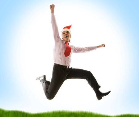 Image of joyful man wewaring santa cap jumping over blue background with green grass beneathの写真素材