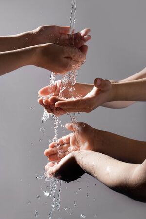 Close-up of six human hands enjoying pure water with open palms on grey backgroundの写真素材
