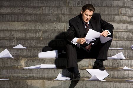 Portrait of depressed employee sitting in frustration on stairs with papers in handsの写真素材