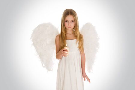 Portrait of innocent girl with candle and wings surrounded by holy light looking at cameraの写真素材