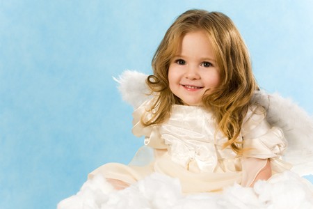 Happy little girl wearing angel dress sitting on white cloud and smilingの写真素材