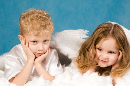 Photo of small boy and girl in angel dresses lying on white cloud and having restの写真素材