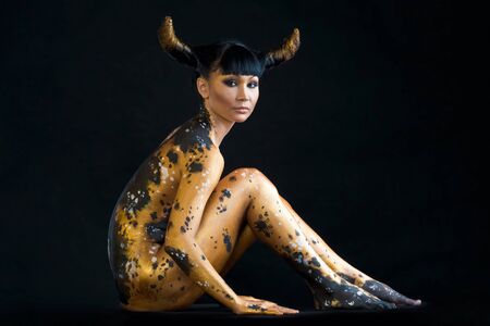 Image of attractive female with painted body sitting over black backgroundの写真素材