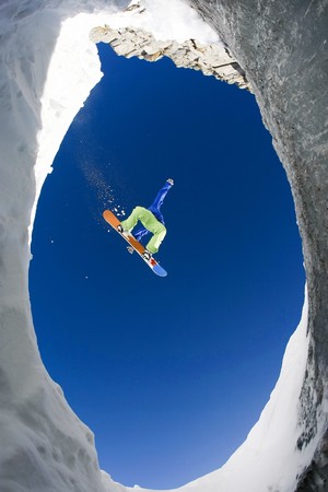 Below view of extreme snowboarder surrounded by rocky mounts covered with snowの写真素材