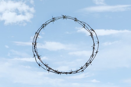 Photo of thorny wreath made of barbed wire on background of blue sky