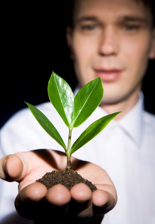 Vertical image of green sprout in pile of soil held by male’s hand