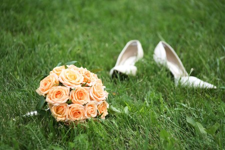 Close-up of bridal yellow rose bouquet on background of her white shoes on green grassの写真素材