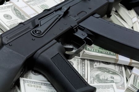 Close-up of black weapon lying on heap of hundred dollar bills