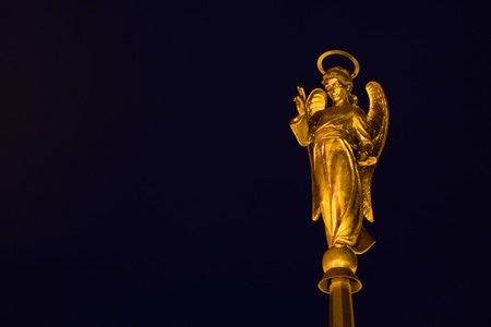 Photo of bronze angel with blessing gesture over black backgroundの写真素材