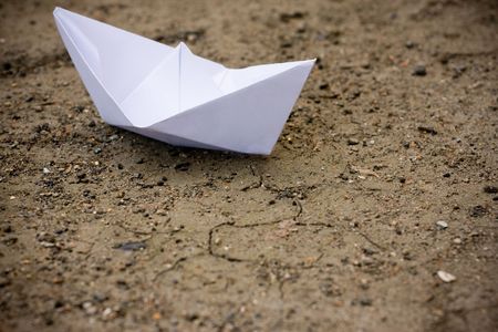 Close-up of paper ship on brown sandy groundの写真素材