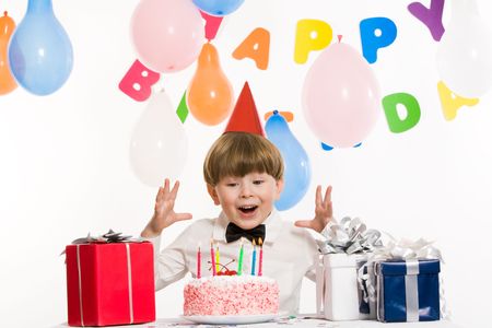 Portrait of surprised lad keeping his hands above birthday cake with burning candles and looking at it astonishinglyの写真素材