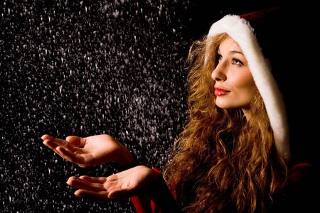 Portrait of pretty girl with open palms catching falling snow over dark backgroundの写真素材