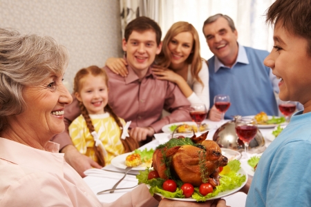 Portrait of happy grandmother holding tray with roasted turkey and looking at her grandsonの写真素材