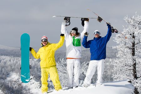 Portrait of three happy young men with snowboards raising their armsの写真素材