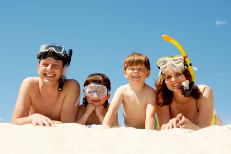 Portrait of diving family lying on sand against blue sky and smiling at cameraの写真素材