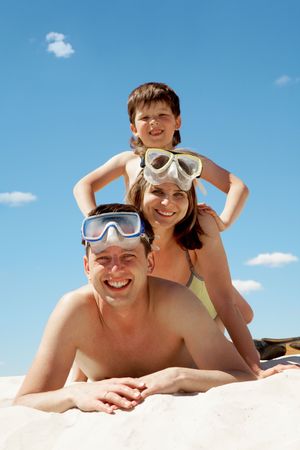 Portrait of cheerful couple in goggles and their son lying on sandの写真素材