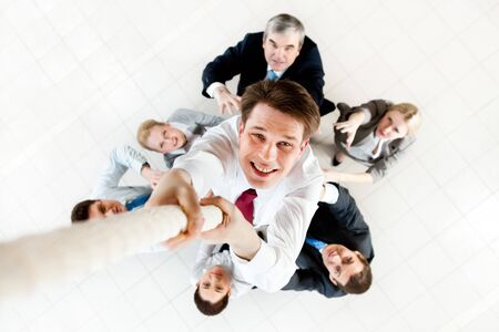 Image of businessman ascending up the rope with business people trying to stop himの写真素材