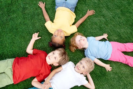 Image of little boys and girls lying on green grass and looking upの写真素材