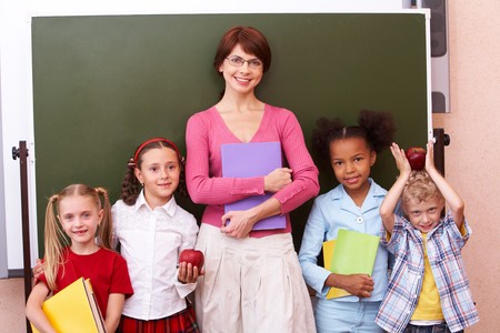 Line of cute schoolchildren looking at camera with their teacher in the middle の写真素材