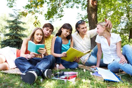 Portrait of teens talking and reading books in park at summerの写真素材