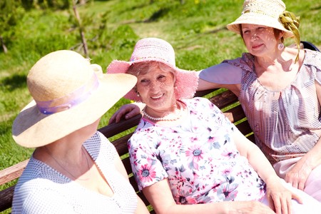 Portrait of three senior females sitting on bench at summer and chattingの写真素材