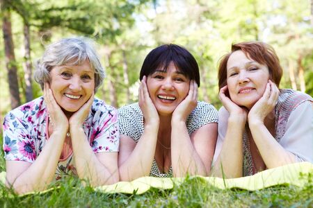 Portrait of three aged women resting on grass and looking at camera with smilesの写真素材