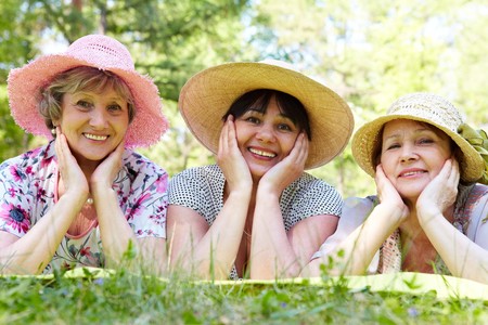 Portrait of three aged women in elegant hats resting on grassの写真素材