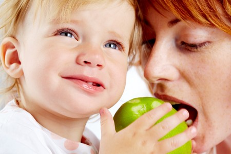 Portrait of female ready to bite ripe apple in her child handsの写真素材