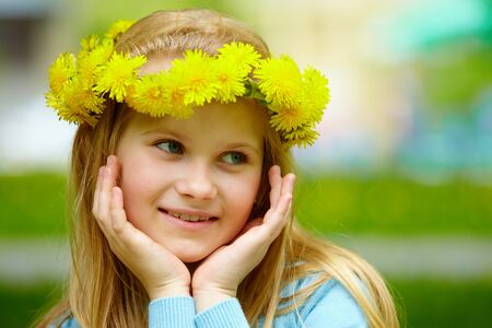 Close-up of cute girl with dandelion wreath posing on summer dayの写真素材