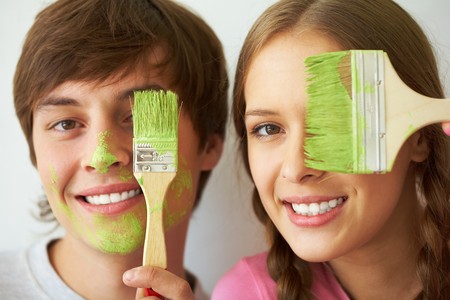 Image of joyful couple hiding one of eyes behind paintbrush with green colorの写真素材