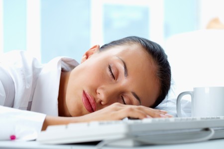 Image of young businesswoman sleeping on workplace with her head on keyboardの写真素材