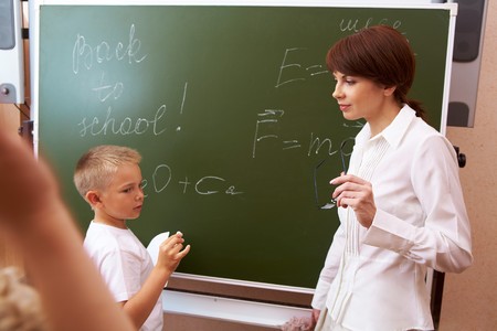  elementary student writing formulae on blackboard with his teacher near byの写真素材