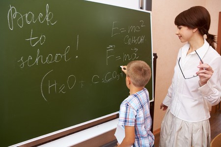  elementary student writing formulae on blackboard with his teacher near byの写真素材