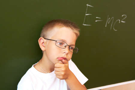 pensive lad by the blackboard touching his chin while thinking of difficult formulaの写真素材