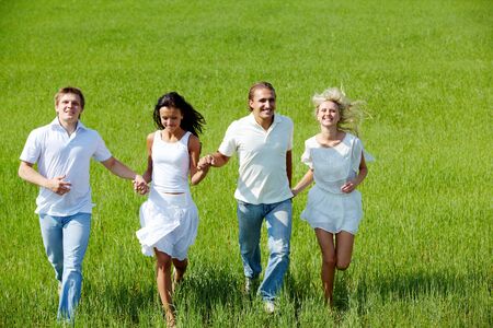 Portrait of happy girls and guys running down green grass on summer dayの写真素材