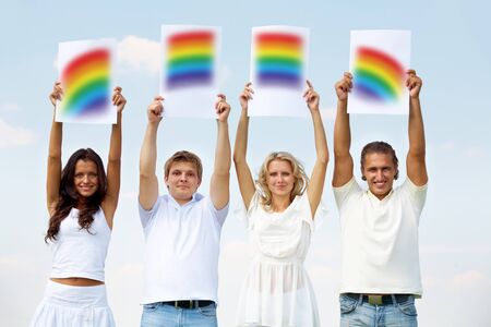 Portrait of happy girls and guys holding papers with rainbow parts outsideの写真素材