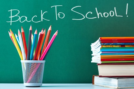 Stack of colorful textbooks and copybooks with pencils near by on background of blackboard