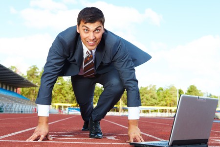 Image of businessman getting ready for race with laptop near byの写真素材