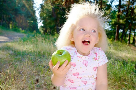 Portrait of cute girl with fair hair eating green apple outdoorsの写真素材
